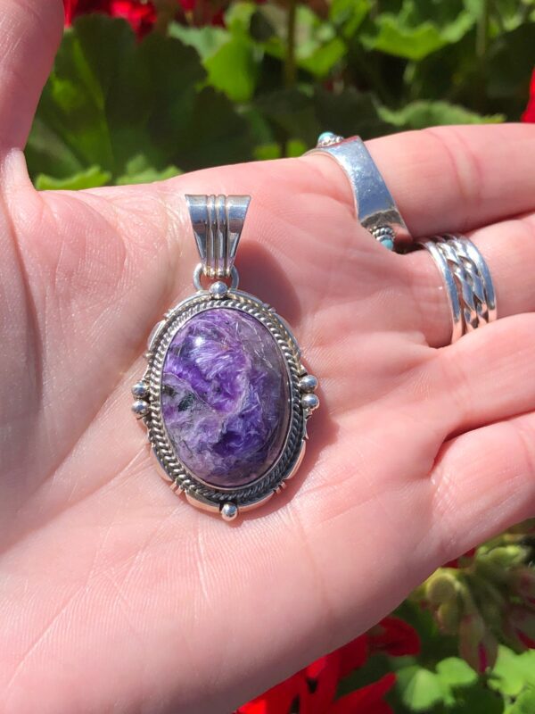 A hand holding a silver pendant with a purple stone.