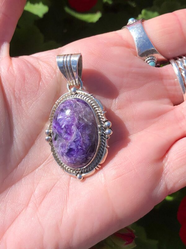 A hand holding a silver pendant with a purple stone.