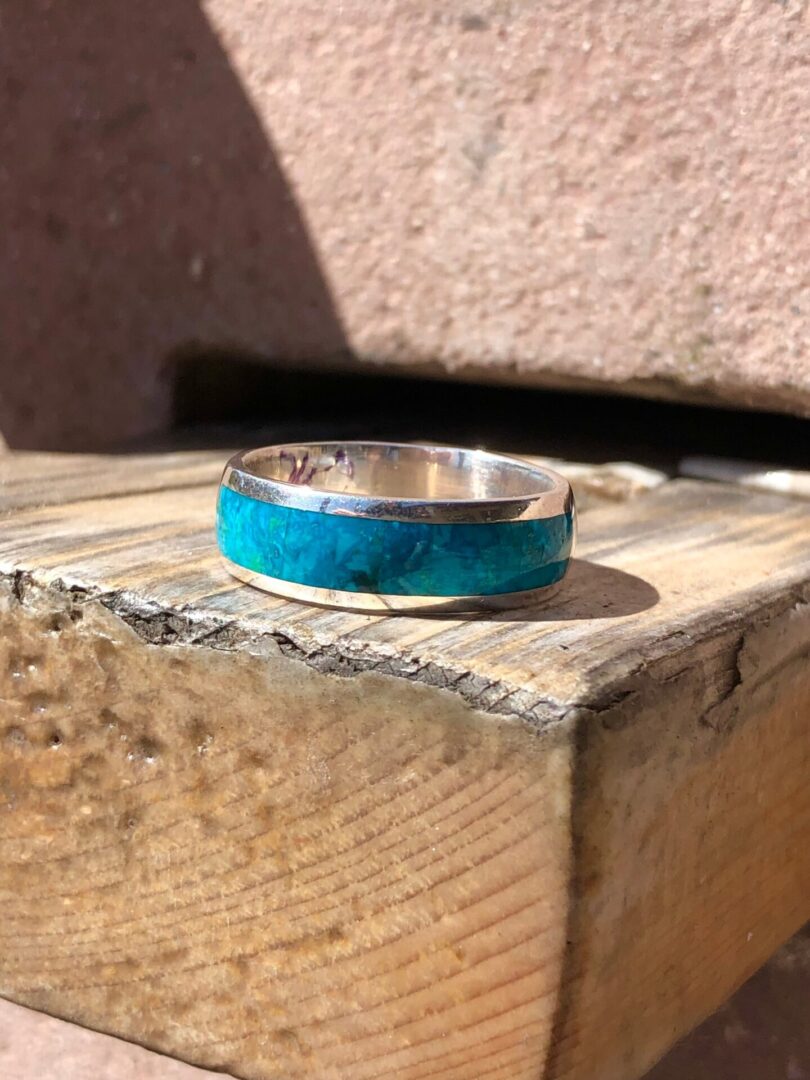 A silver ring with turquoise inlay sitting on top of a wooden bench.