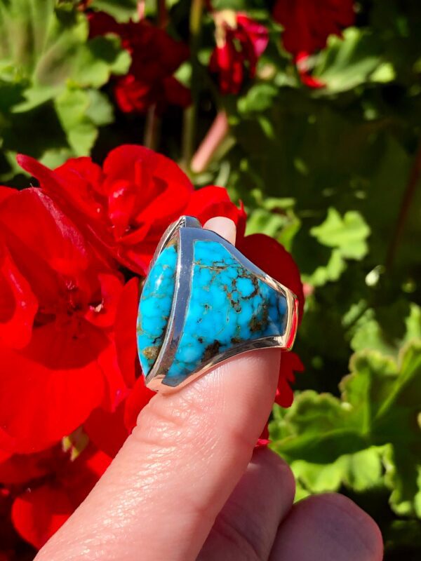 A turquoise ring with silver setting on a finger.