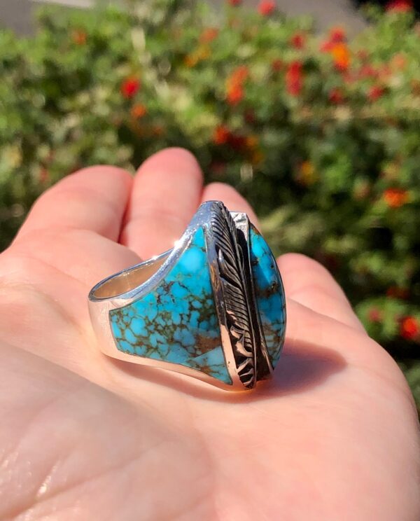 A hand holding a turquoise and silver ring.