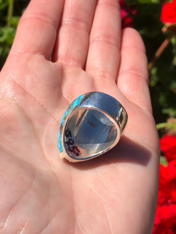 A hand holding a silver ring with a turquoise stone.