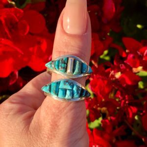 A hand holding a ring with a turquoise stone.