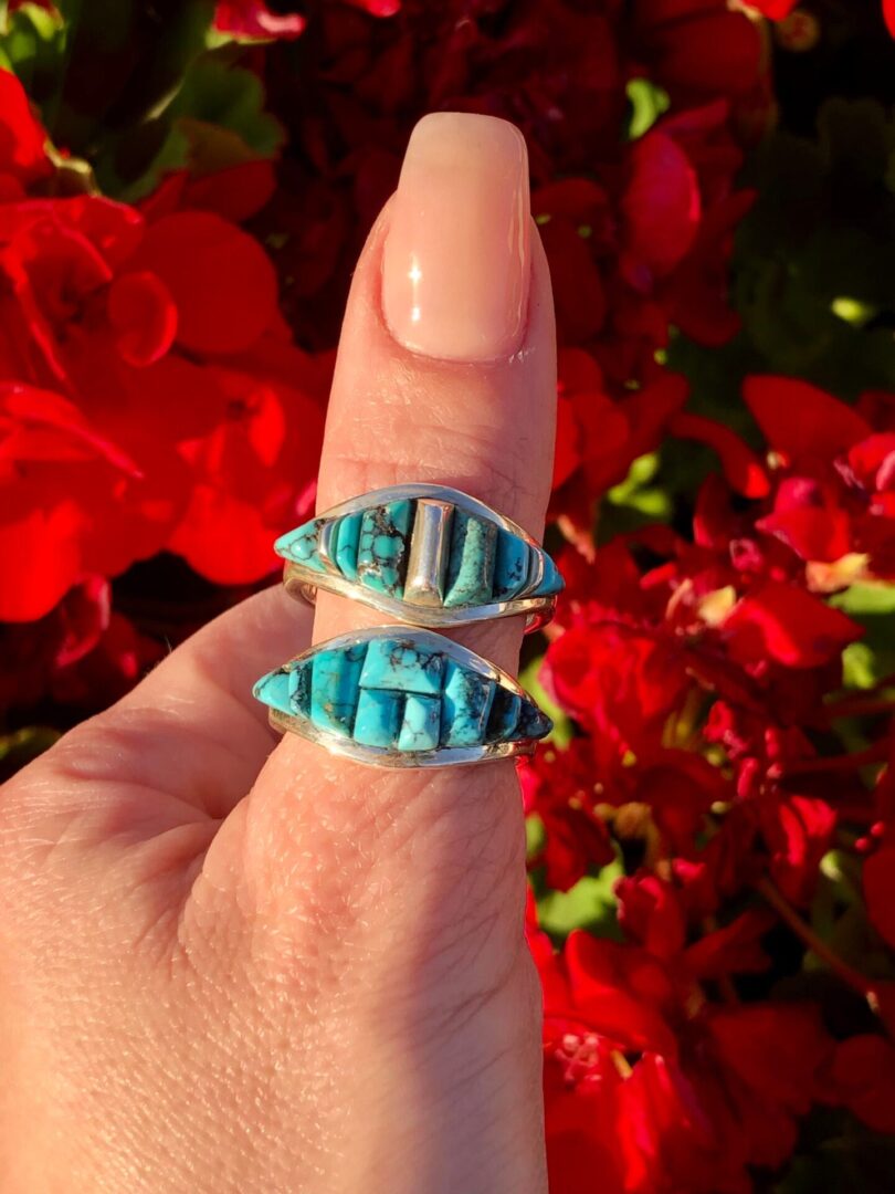 A hand holding a ring with a turquoise stone.