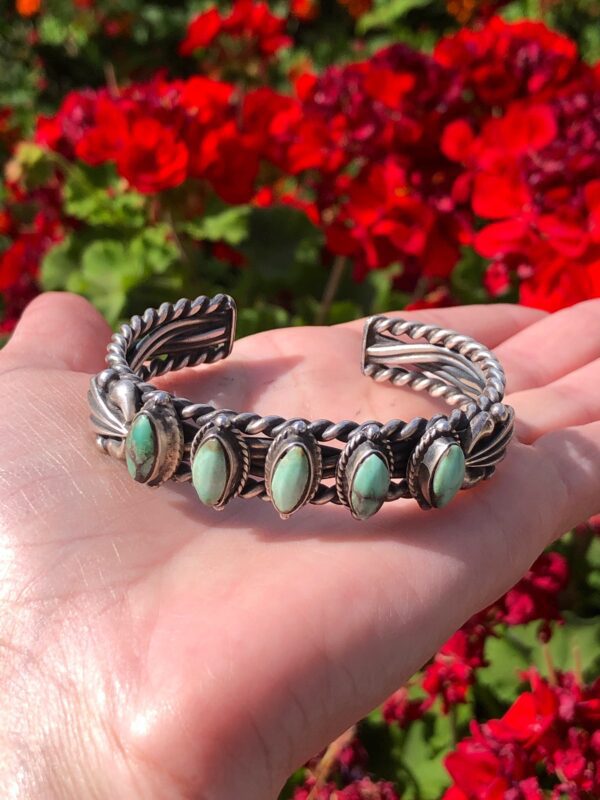 A hand holding a bracelet with turquoise stones.