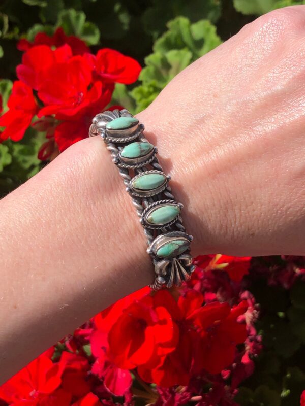 A woman's hand is holding a bracelet with turquoise stones.