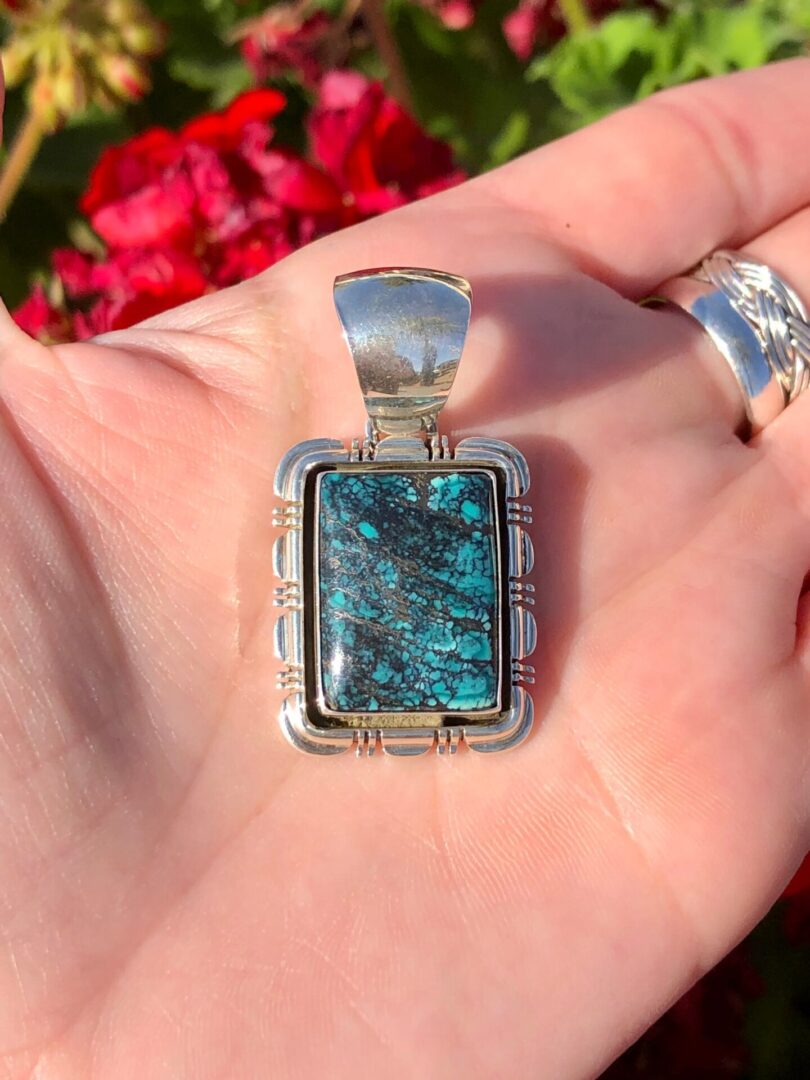 A person holding a square turquoise stone pendant.