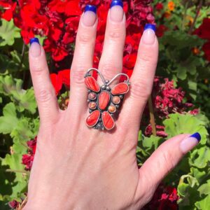 A hand holding a ring with a red butterfly on it.
