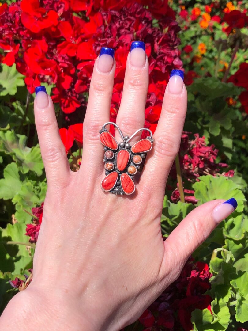 A hand holding a ring with a red butterfly on it.