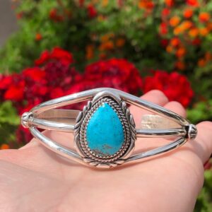A person holding a bracelet with a turquoise stone.