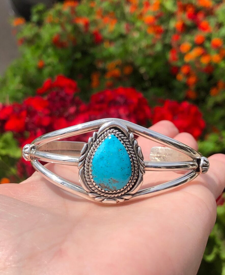 A person holding a bracelet with a turquoise stone.