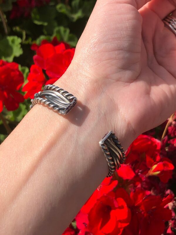 A woman's hand is holding a pair of silver cuff bracelets.