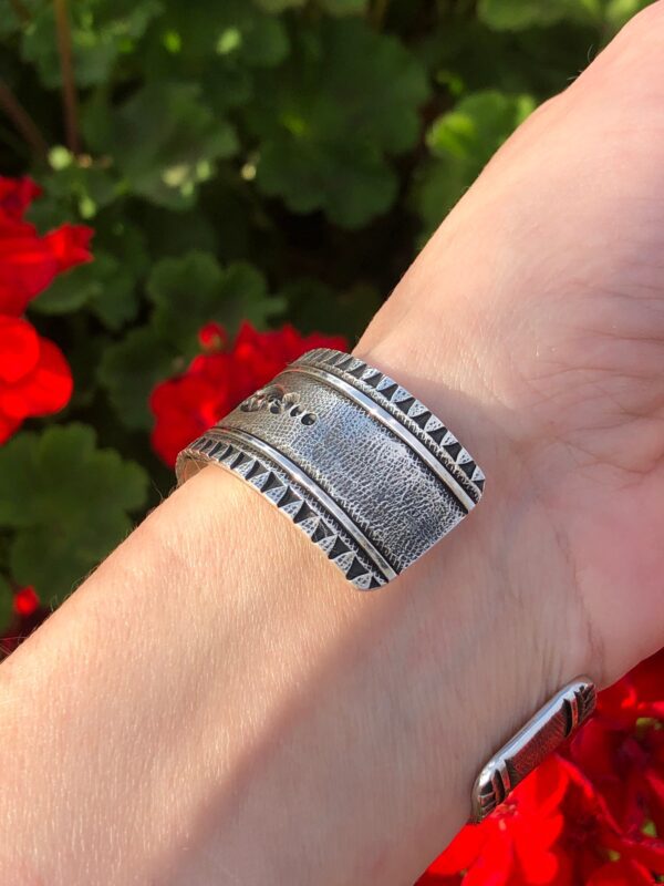 A silver cuff bracelet with a textured surface and stamped design.