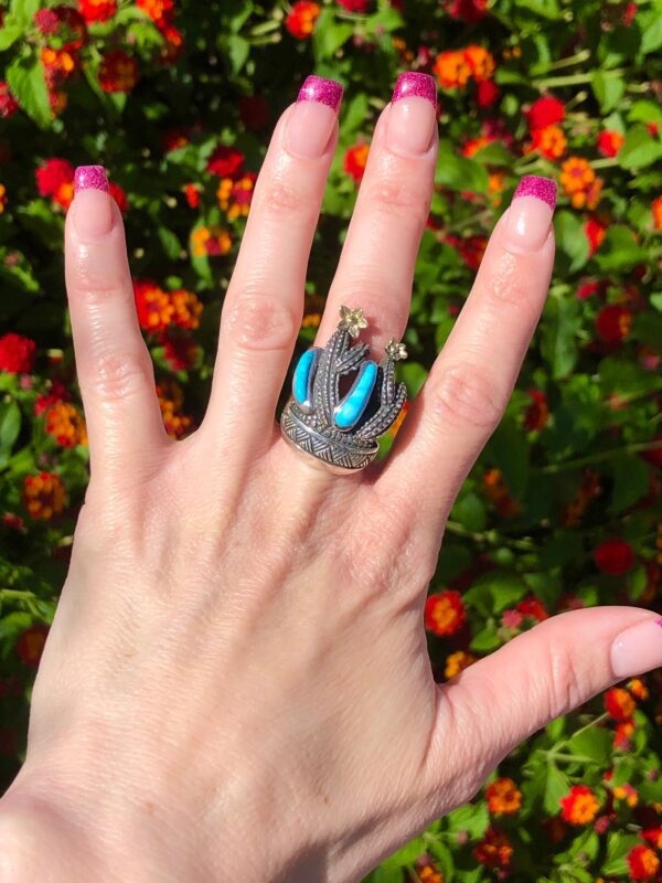 Cactus ring with blue stones on a hand with pink nails.