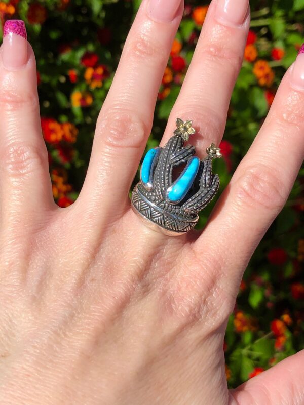 A hand wearing a silver ring with a cactus design.