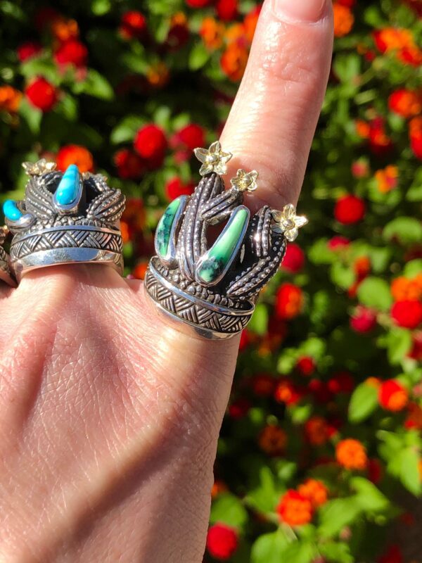 A hand wearing two silver rings with green and blue stones.