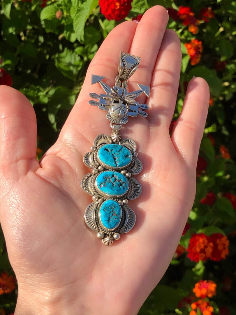 A hand holding a pendant with a turquoise stone.