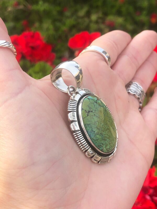 A hand holding an oval green stone pendant.