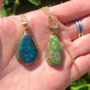 A hand holding the 14KT GOLD AAA Grade Kingman Turquoise + Lime Green Carico Lake Turquoise Navajo Handmade Solid Gold Pendents/Gold Native American jewelry with different colored stones.