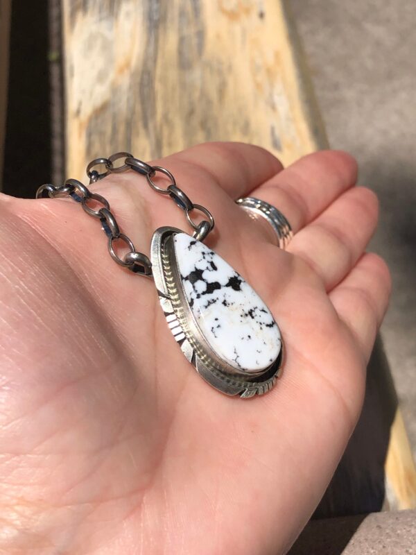 A hand holding a silver pendant with a white stone.