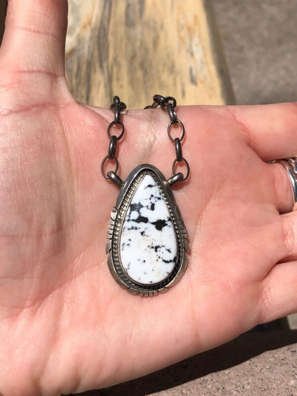 A hand holding a silver pendant with a white stone.