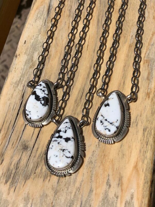 Three pendants with white and black stones on silver chains.