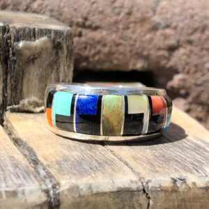 A ring with multi colored inlay on top of a wooden board.