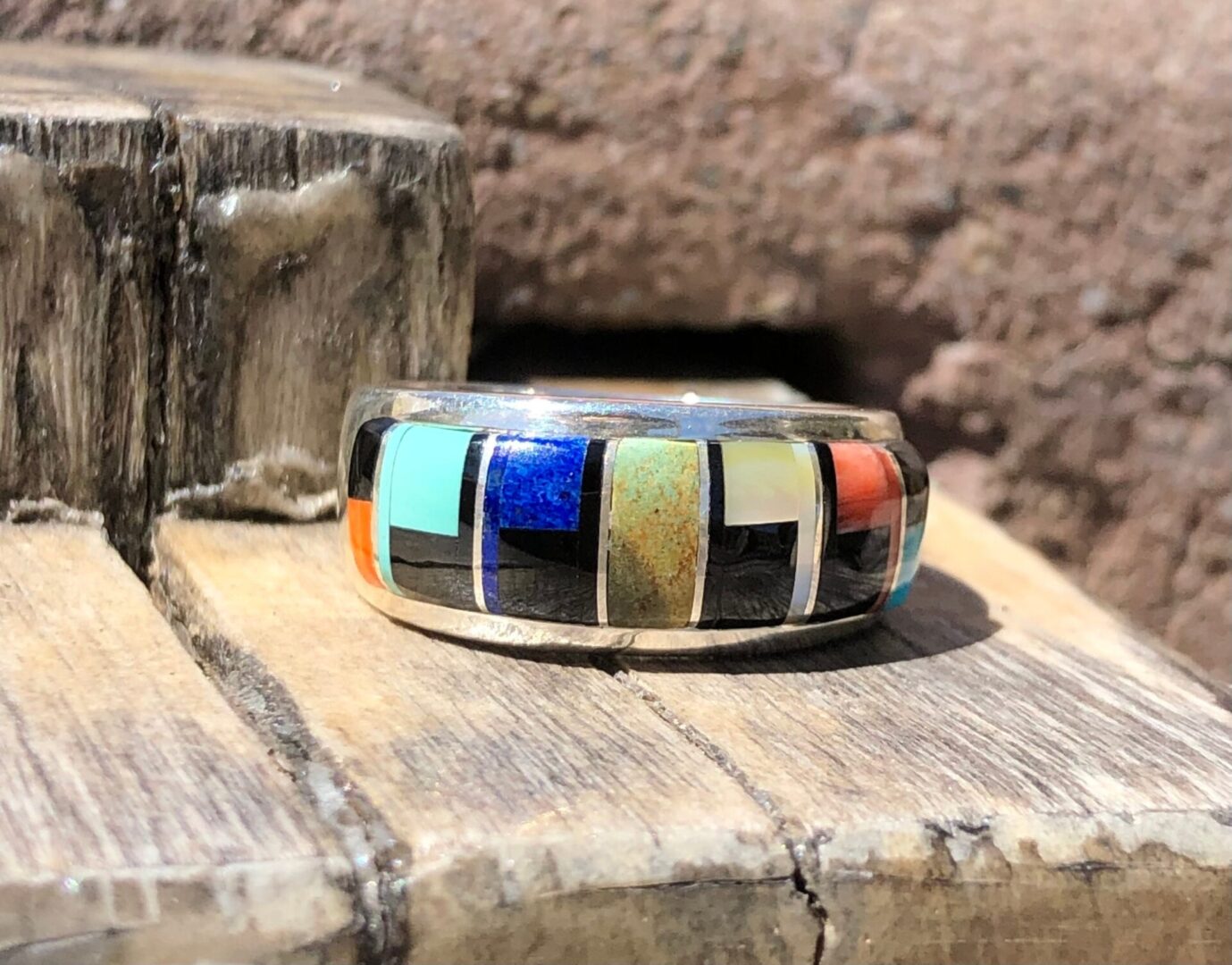 A ring with multi colored inlay on top of a wooden board.