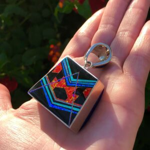 A hand holding a square pendant with geometric inlay.