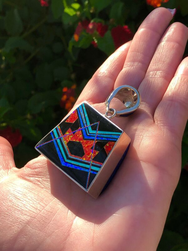 A hand holding a square pendant with geometric inlay.