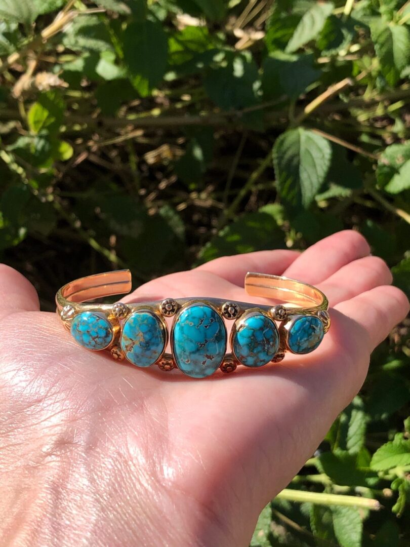 A person holding a turquoise cuff bracelet.