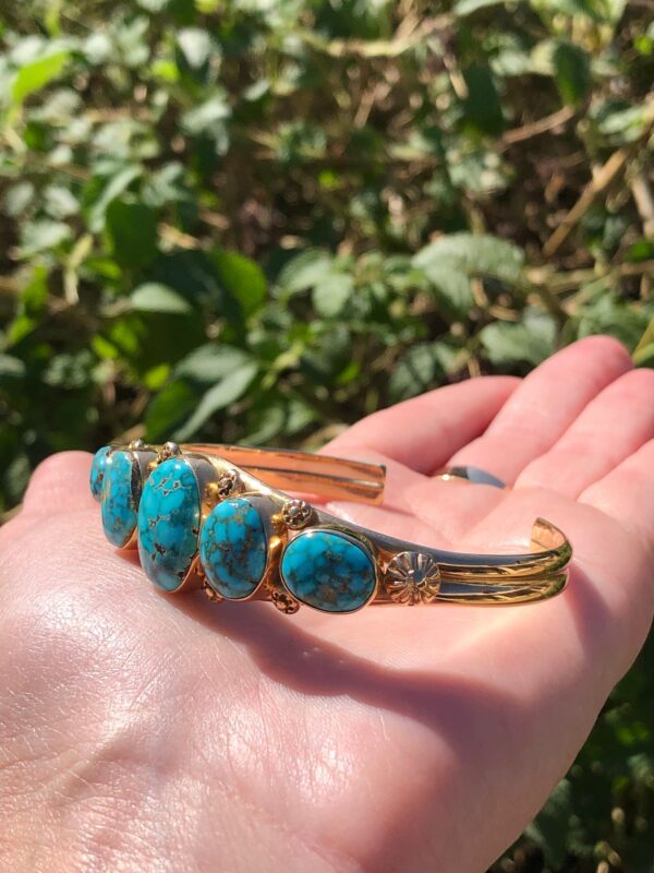 A person's hand holding a turquoise cuff bracelet.