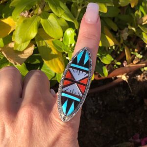 A person is wearing a Native American style ring with turquoise, coral, and onyx inlay.