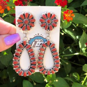 A hand holding a pair of red coral earrings.