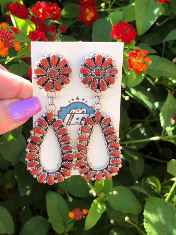 A hand holding a pair of red coral earrings.