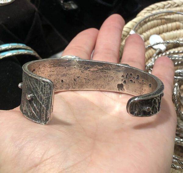 A person's hand holding a silver cuff bracelet.