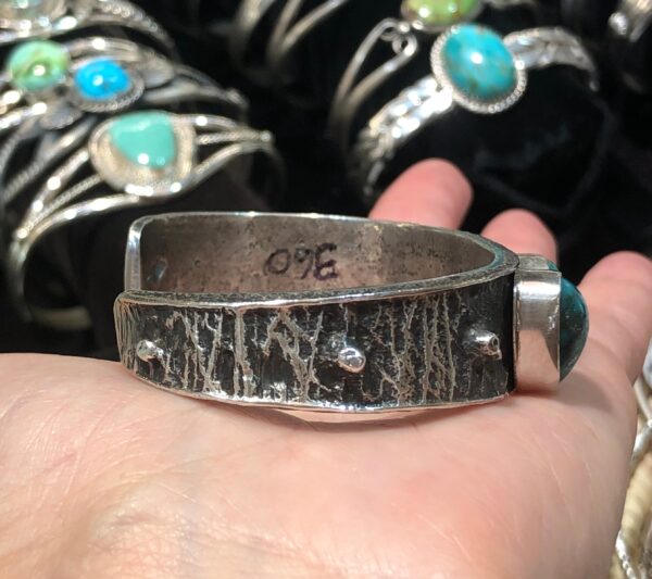 A person is holding a silver cuff with turquoise stones.