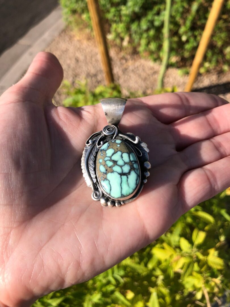A hand holding a pendant with a turquoise stone.