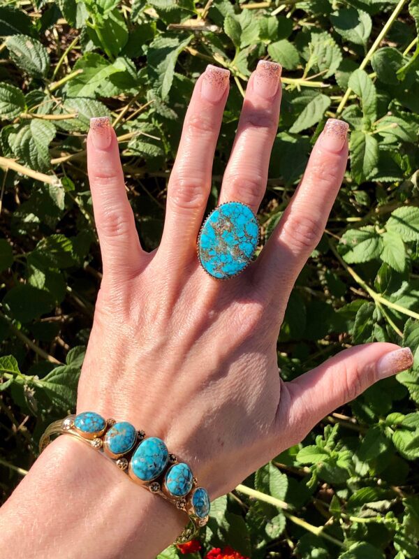 A woman's hand holding a turquoise stone ring.