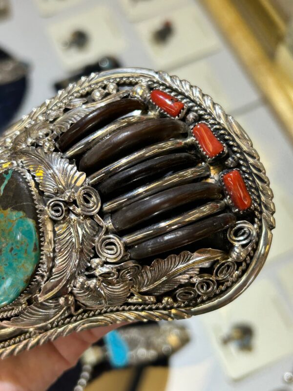 A person is holding a silver belt with turquoise and coral.