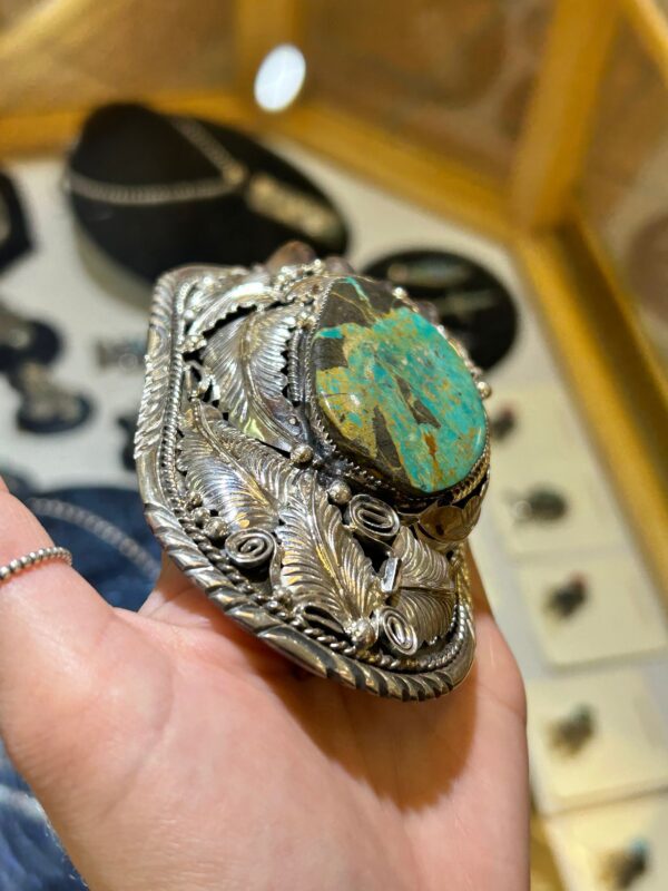 A hand holding a turquoise and silver brooch.