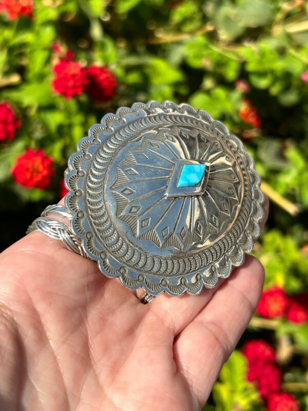 A hand holding a silver and turquoise belt buckle.