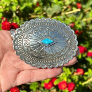 A hand holding a silver belt buckle with a turquoise stone.