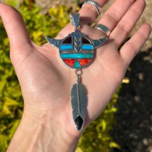 A hand holding a pendant with a feather and inlay.