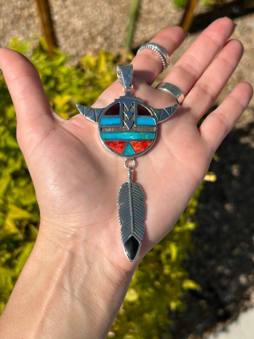 A hand holding a pendant with a feather and inlay.