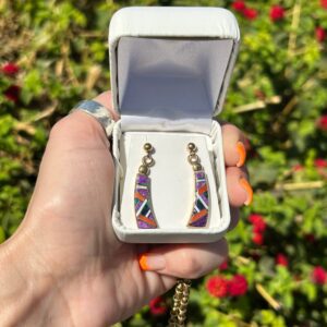 A hand holding a pair of earrings in a white box.