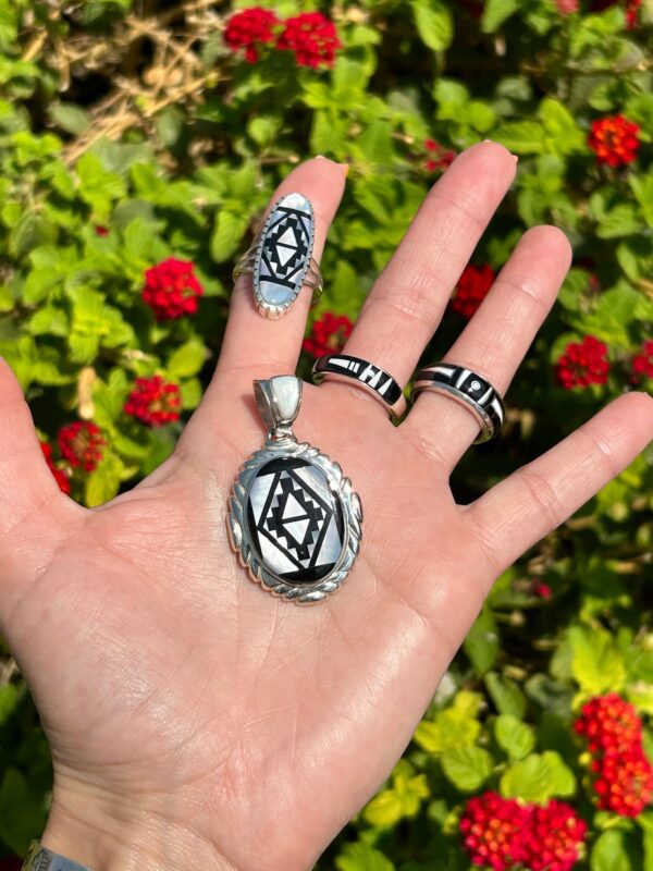 A hand holding a silver and black pendant and two rings.