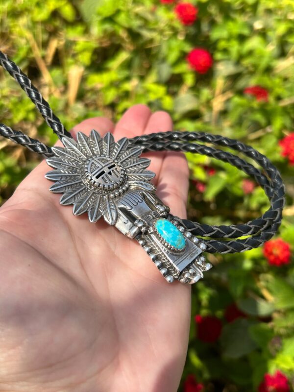 A person is holding a silver and turquoise necklace with a sun on it.