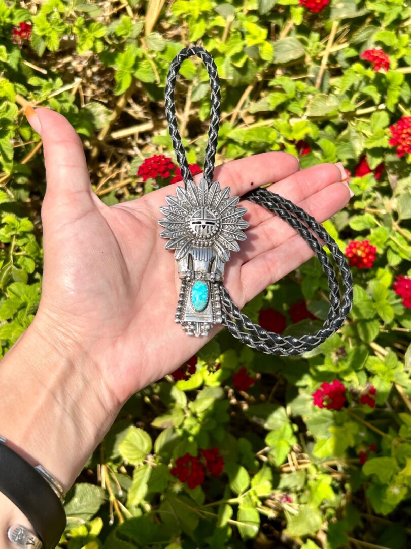 A person holding a necklace with a turquoise stone.