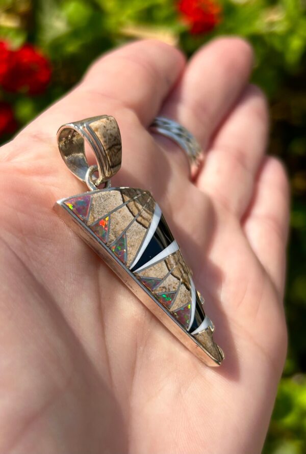 A hand holding a silver pendant with colorful inlays.